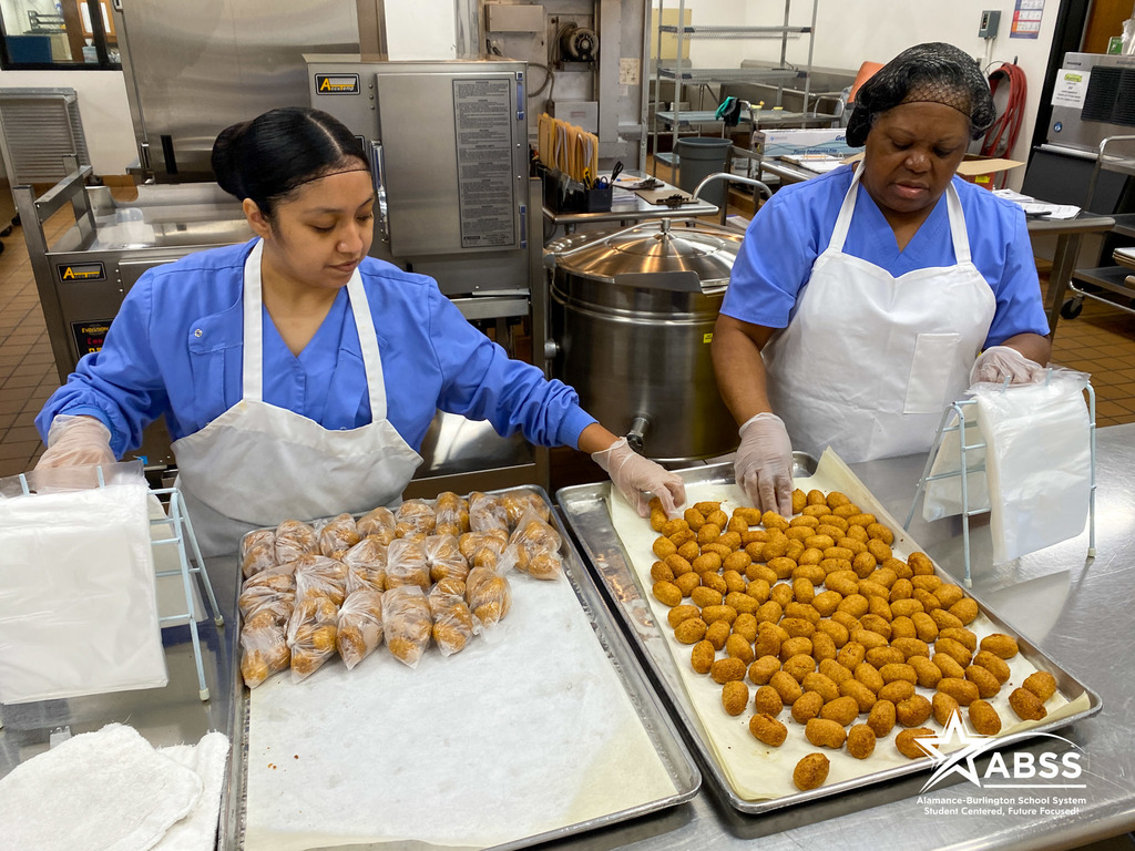 Two school nutrition staff sort corn dog nuggets on a tray into clear plastic bags