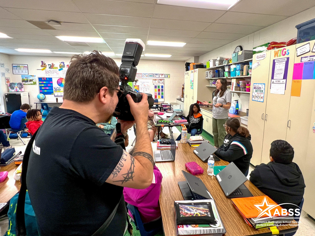 A photographer focuses on a teacher leading her third grade class in discussion