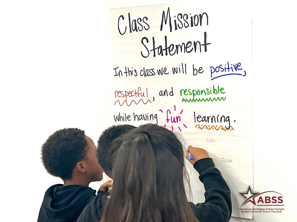 Third grade students write their name on a mission statement poster