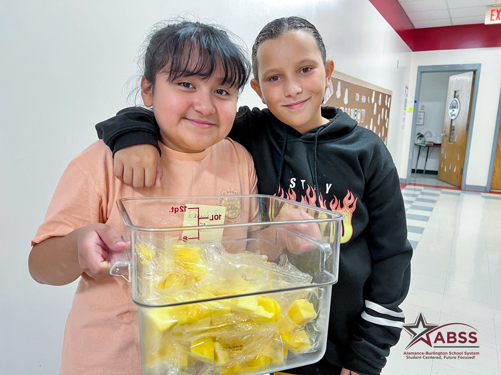 Two elementary students hold a bucket of mango pieces