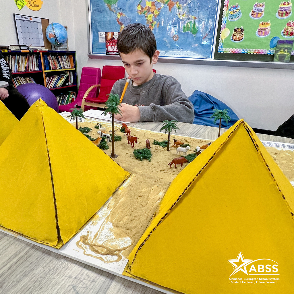 A student writes down notes in front of his large Egyptian pyramid diorama