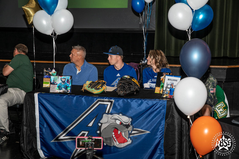 Cole McGinnis - UNC Asheville - Baseball seated with his family at the table with UNC Asheville banner draped over front 