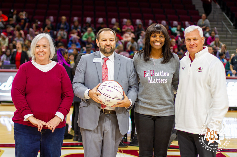 Superintendent Dr. Dain Butler stands with Dean of Education, Women's Basketball coach, and holds a signed basketball