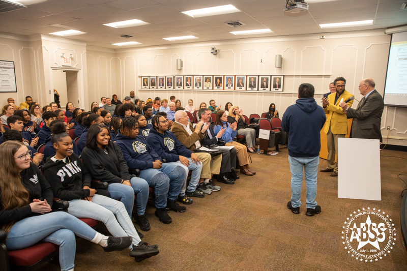 Image of band in audience clapping as presentation is made.  Students sitting in board room auditorium wearing matching sweatshirts with Cummings Band and Broadview Band logos on front