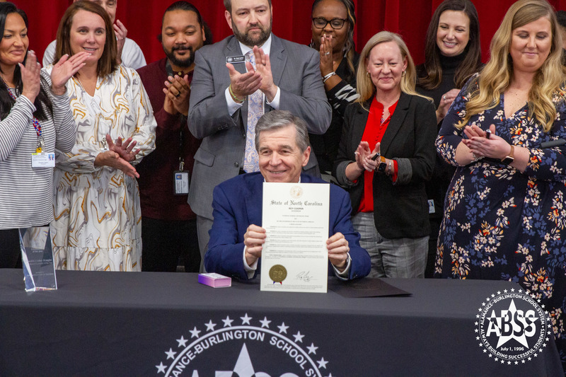 Governor Roy Cooper holds up a proclamation signed in front of a BSS, counselors, principal, TerrGovernor Roy Cooper holds up a proclamation signed in front of ABSS, counselors, principal Terri Drummond, and superintendent Dain Butler