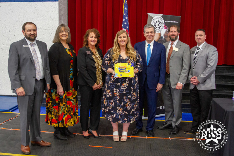 Roy Cooper stands with superintendent Dain Butler, and national school counselor of the year Meredith Draughn and school board members