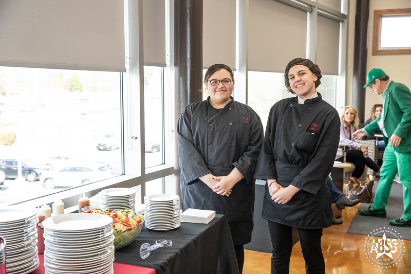 Culinary students from CTEC posing with their culinary arts outfits by buffet table. 