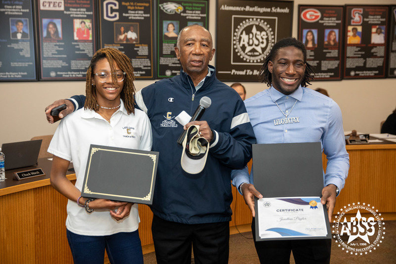 Group photograph of student athletes Jonathan Paylor and Deanna Cotton holding their certificates and standing beside Cummings High School track and field coach 