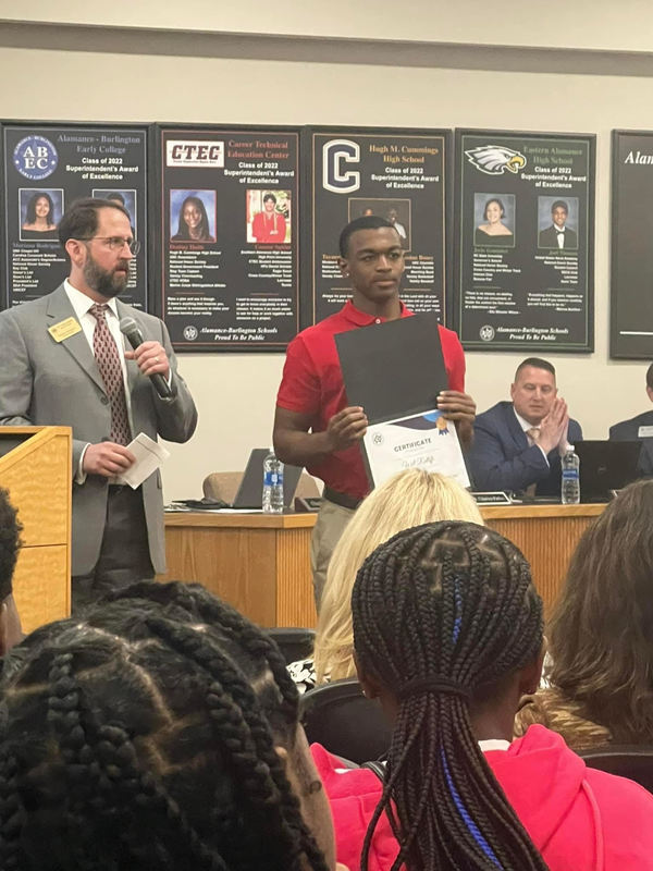 Photograph of student athlete Will Ratliff holding his certificate in front of Board of Education with Board Member Dr. Charles Parker congratulating him.