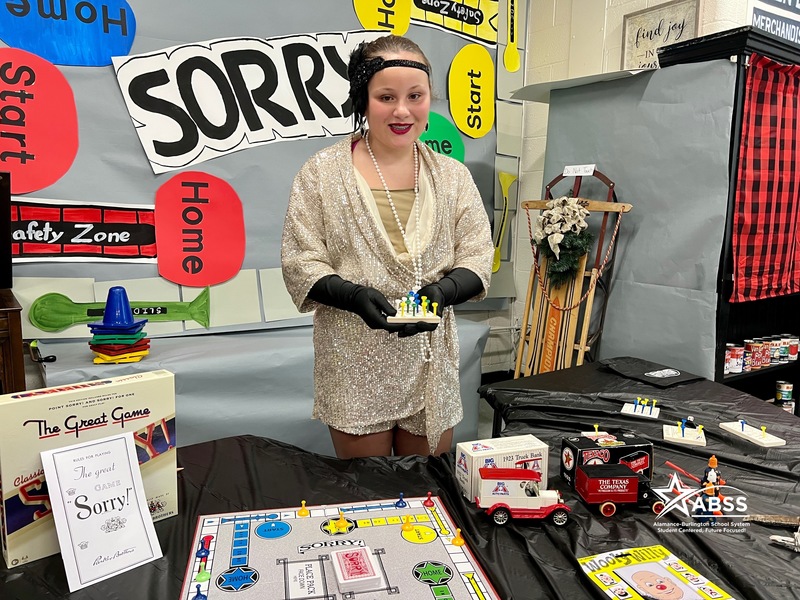 Student in decade room showing off toys from 1920s dressed in 1920s attire. 