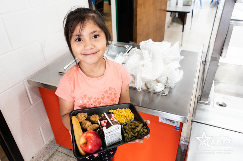 student holding lunch tray showing off fresh fruit and vegetables. 